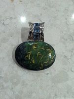 Front view showing green cabochon and bail with blue rhinestones
