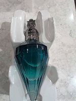 Full view of teal jewel-shaped perfume bottle in white insert