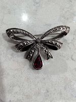 Front view of silver-tone bow brooch showing rhinestones and red drop stone