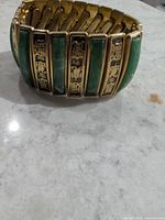 Full view of bracelet showing alternating green panels and gold-tone symbol panels