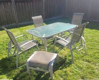 full view of patio set showing glass table, five chairs, one ottoman on lawn