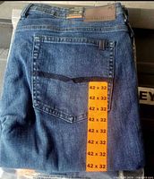Folded blue denim jeans in plastic with size sticker 42x32 visible