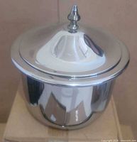 Lidded stainless steel bowl on box, showing exterior finish and lid with finial