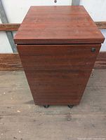 Front view of the cabinet showing wood finish, lock and casters