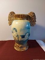 Front view showing cherub images, gold wing handles, ruffled rim, and ornate base