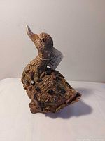 Left side view of composite duck figurine showing pebble inlays and original tag string