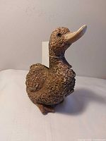 Front left view of textured brown duck figurine, tag visible