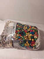 Overview of sealed bag showing multicolour wooden beads, faux pearl strand and assorted jewelry pieces