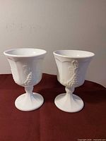 Two milk glass goblets standing upright showing grape pattern