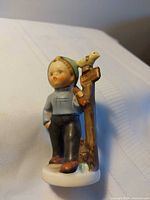 Front view of ceramic boy figurine beside post with bird