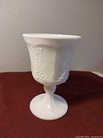 Straight-on view of milk glass goblet showing flared rim and grape relief