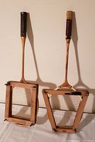 Two wooden badminton rackets each inside wooden press frames standing upright