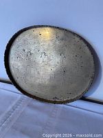 Front view of oval brass tray showing engraved figures and scalloped rim