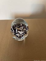 Front view of clear egg-shaped paperweight showing internal purple and white swirl and bubbles