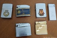 Front view of six vintage pocket lighters showing designs and finishes