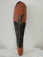 Front view of elongated wooden Fang mask showing red and black painted surfaces and facial details