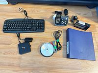 Full lot overview on floor displaying keyboard, phone, TV box, clock, cables, CD spindle, binder