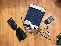 Top view of navy Conair massager pad, controller, power adapter and two black braces on floor