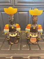 Front view of both brown glass figural decanters with yellow sombrero stoppers, one showing Old Oak Rum label