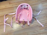 Full view of pink booster seat with straps displayed on floor