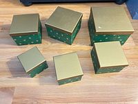 Six green boxes with gold lids arranged by size