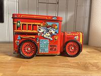 profile view of red fire truck tin showing printed Dalmatian firefighters and wheel detail