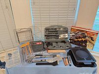 Overall lot layout showing tool set, griddle plate, baskets, utensils, skewers and grill cover