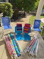 Lot overview: two blue beach chairs, two upright chairs partially visible, striped towels, five packaged umbrellas