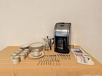 Overall lot showing coffee maker, moka pot, dinnerware stacks and flatware on table