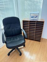 Overall view of black office chair, wooden mail sorter, small drawer unit