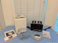 Bread maker, toaster, two chrome baskets and manuals on tabletop