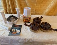 Lot overview showing three crocks with lids, onion machine components, bloom maker box, cookbook
