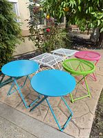 Six folding metal patio tables arranged outdoors showing colors and styles