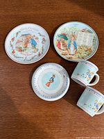 Overview of five Wedgwood Peter Rabbit pieces: three plates and two mugs