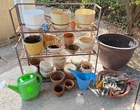 Front view of rack filled with assorted pots, large resin planter to right, watering cans and tools in foreground