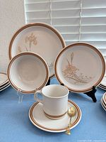 Place setting showing dinner plate, bowl, mug, saucer, floral pattern and gold spoon