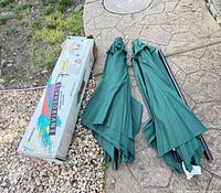 Two folded green umbrellas with pole sections beside boxed gazebo shade