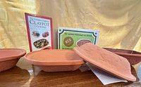 Two terracotta roaster bases, lid, cookbook and packaging displayed