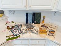 Entire lot displayed on countertop: apron, mitts, pot holders, packaged towels, tapestry towels, whisk