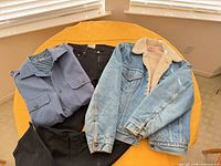 Denim jacket, work shirt, black jeans and blue jeans laid out on table