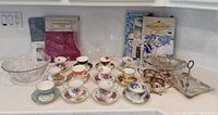 Group shot of teacups, silverplate pieces, glass bowl, packaged linens