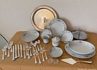 Full lot: china dinnerware, silverplate flatware, trays and serving pieces displayed on table
