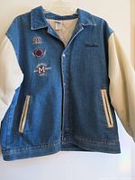 Front view of denim varsity jacket showing body, sleeves, pockets, snap closure, and chest embroidery