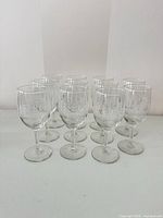 Group of 11 identical etched wine glasses on white surface