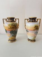 Front view of both Noritake vases showing landscape scene and gilt handles