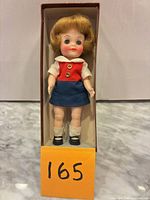 Front view of the 1965 Effanbee 9-inch doll standing inside its cardboard box, showing outfit and shoes