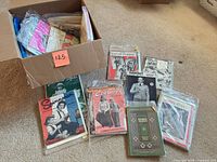 Open box filled with sleeved vintage knitting magazines, several spread out in front