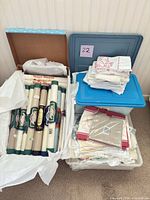 Three containers holding Vinyl-Weave rolls, stacked linens, lace and kits