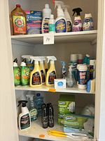 Cabinet shelves filled with various full cleaning product bottles, sprays, cans and Swiffer box