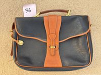 Front view showing two-tone pebbled leather body, tan buckle strap, top handle, shoulder strap hardware and duck fob
